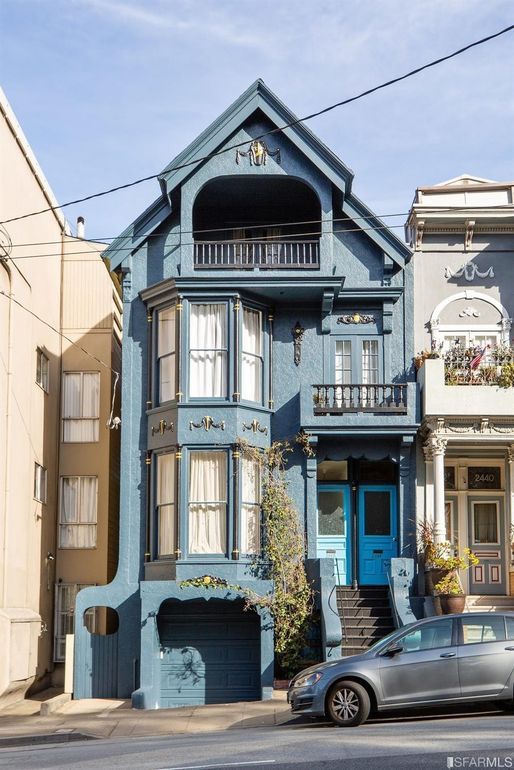 a car parked in front of a blue house on a street with two story houses