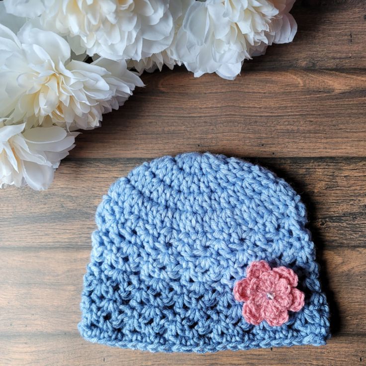 a blue crocheted hat with a flower on it sitting next to white flowers