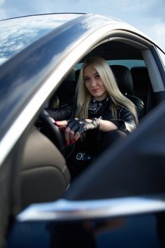 a woman sitting in the driver's seat of a car with her hand on the steering wheel