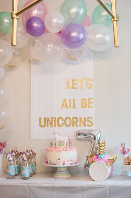 a table topped with lots of balloons and cake next to a sign that says let's all be unicorns