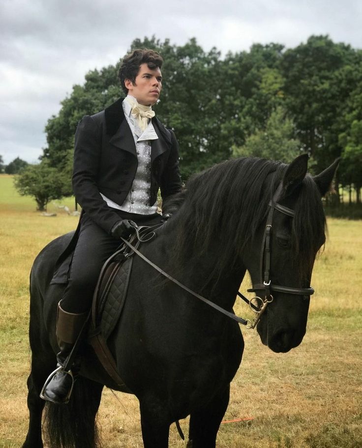 a man riding on the back of a black horse in a field with trees behind him