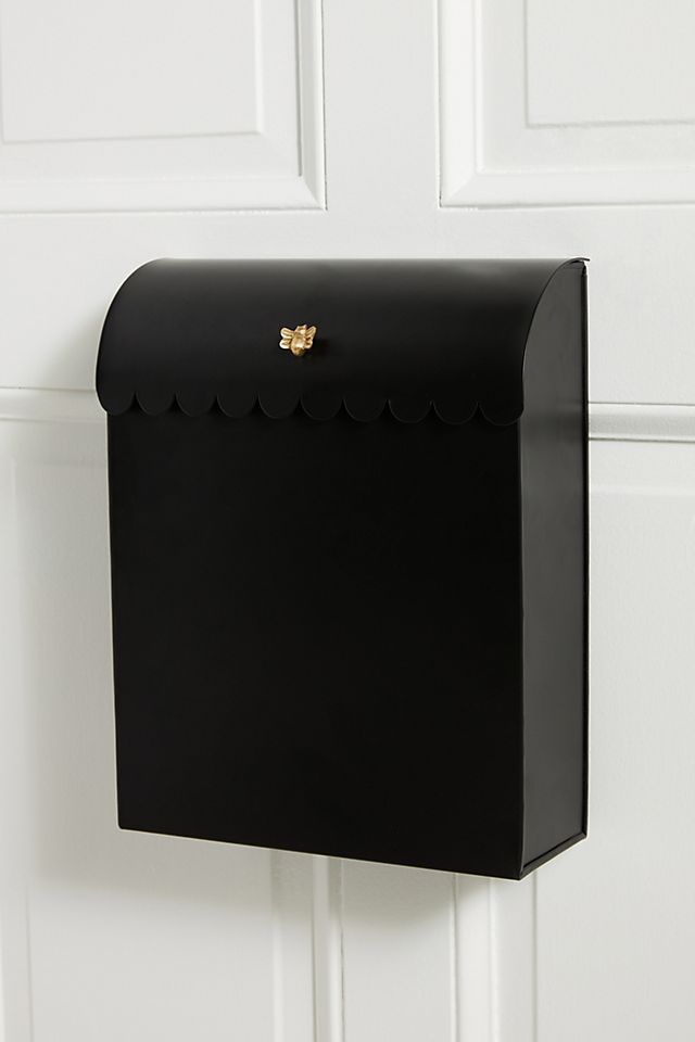 a black mailbox mounted to the side of a white door with scalloped edges