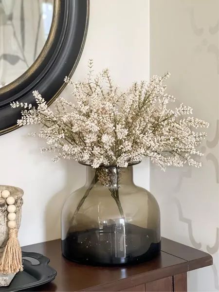 a vase filled with white flowers sitting on top of a wooden table next to a mirror