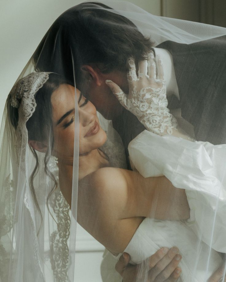 the bride and groom are embracing each other under their wedding veil, in this artistic photo