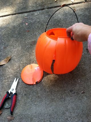 someone is carving a pumpkin out of an orange bowl with scissors on the ground next to it