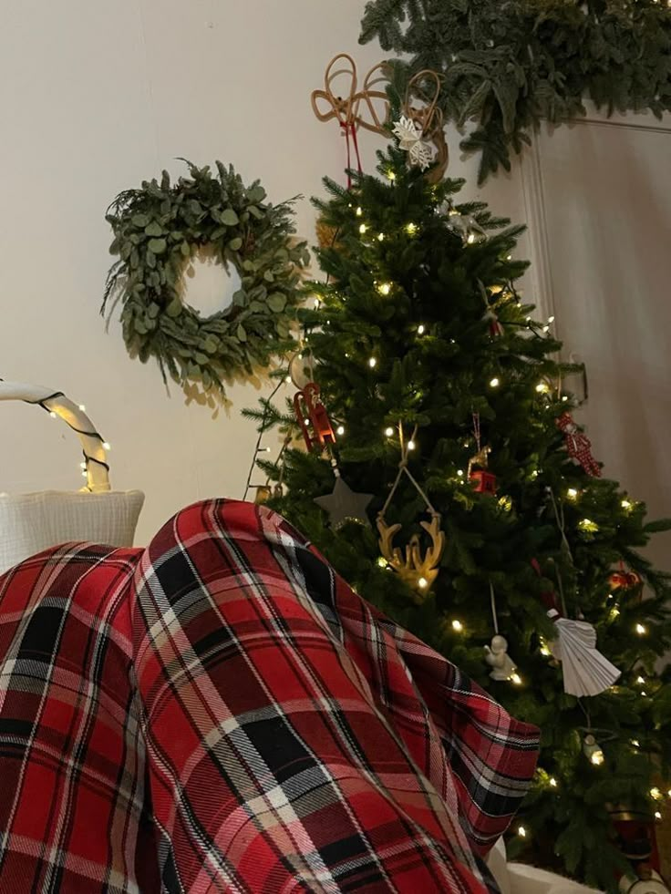 a living room with a christmas tree and plaid blanket on the couch in front of it