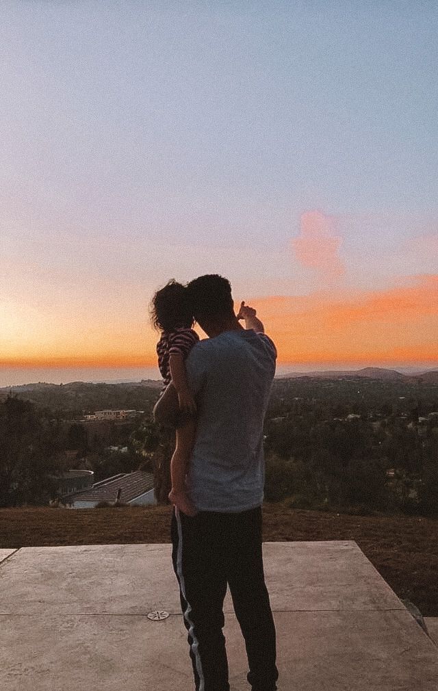 a man holding a small child while standing on top of a cement slab at sunset