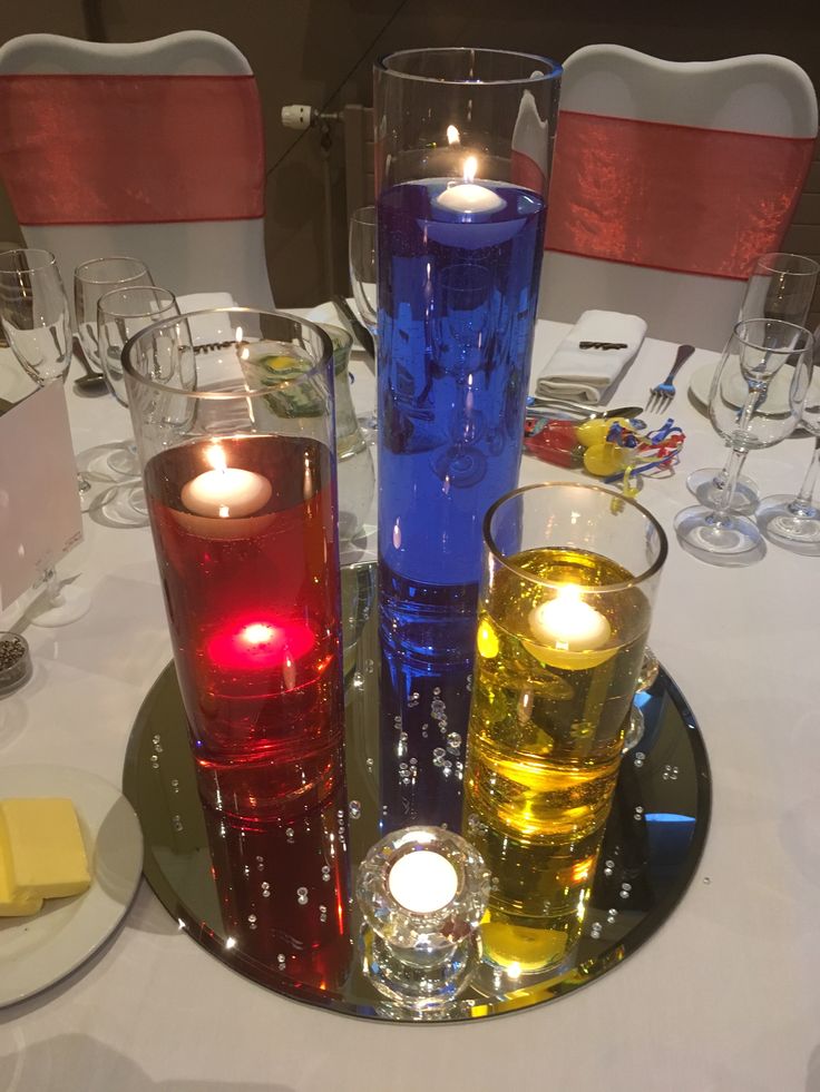 three candles are lit in different colors on a table with white linens and silverware