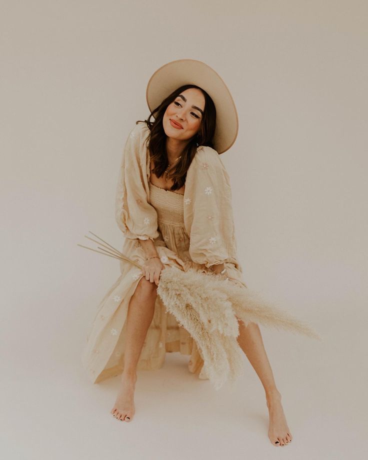 a woman sitting on the ground wearing a hat and dress with feathers around her legs