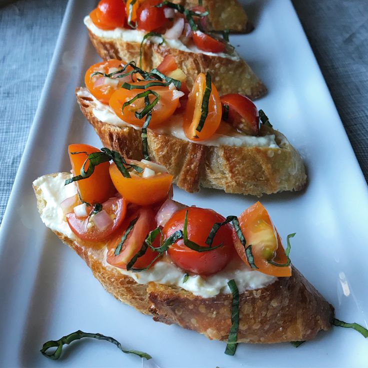 several pieces of bread with tomatoes and cheese on them sitting on a white platter