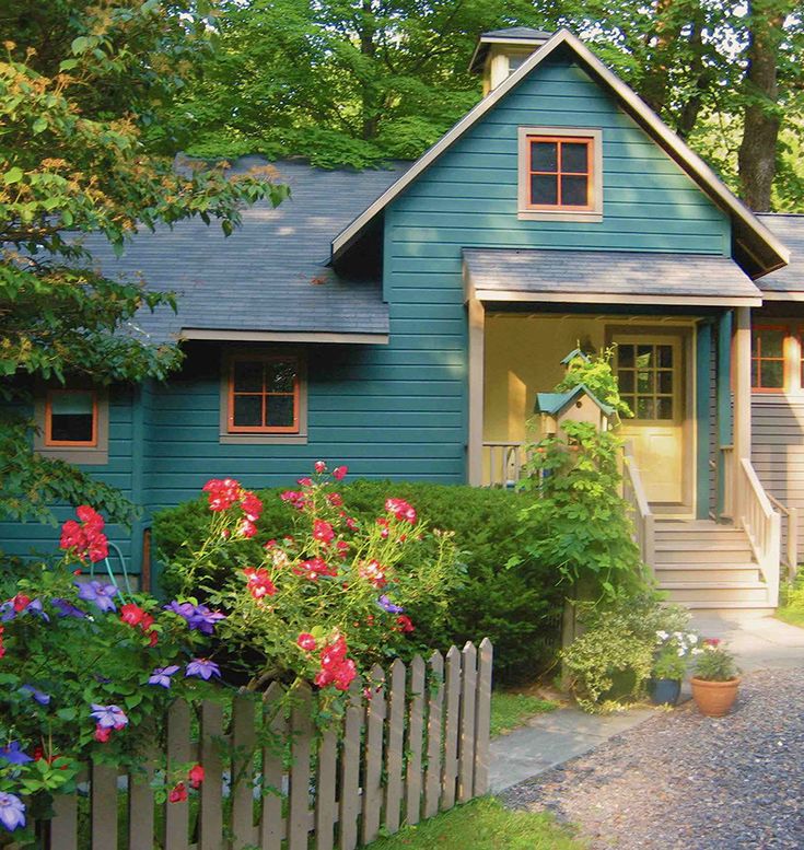 a blue house with flowers in front of it and a wooden fence around the yard