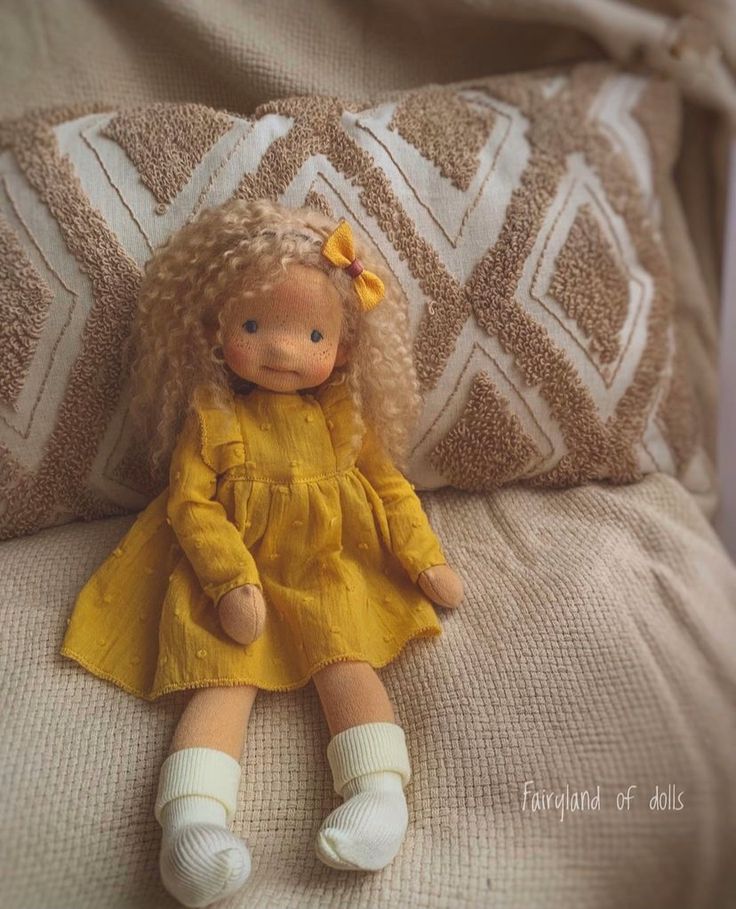 a doll sitting on top of a bed next to a pillow