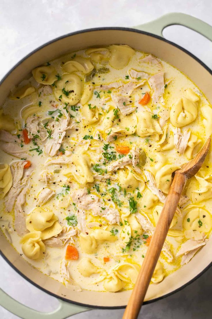 a pot filled with chicken noodle soup and a wooden spoon in the bowl next to it