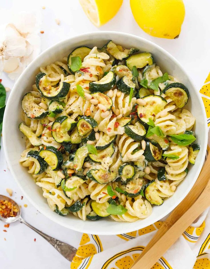 a white bowl filled with pasta, zucchini and spinach on top of a table