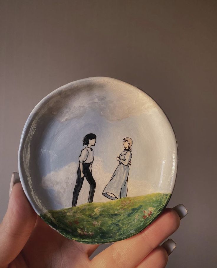 a hand holding a small plate with a drawing of two people standing on top of a hill