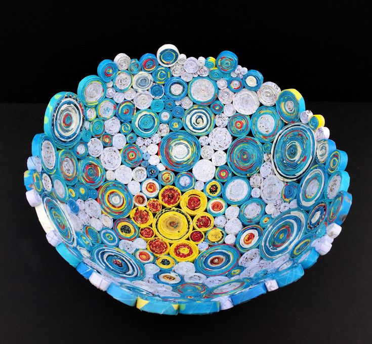 a bowl made out of paper with circles and flowers on the bottom, sitting on a black surface