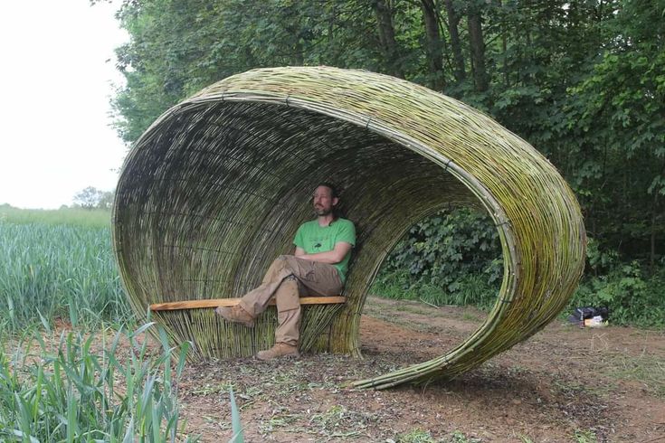 a man sitting on a bench made out of sticks in the middle of a field