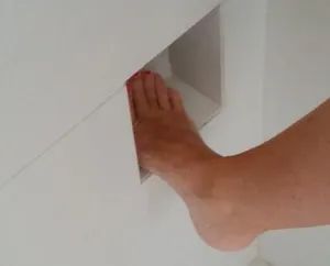 a person's bare foot sticking out of the corner of a room with white walls