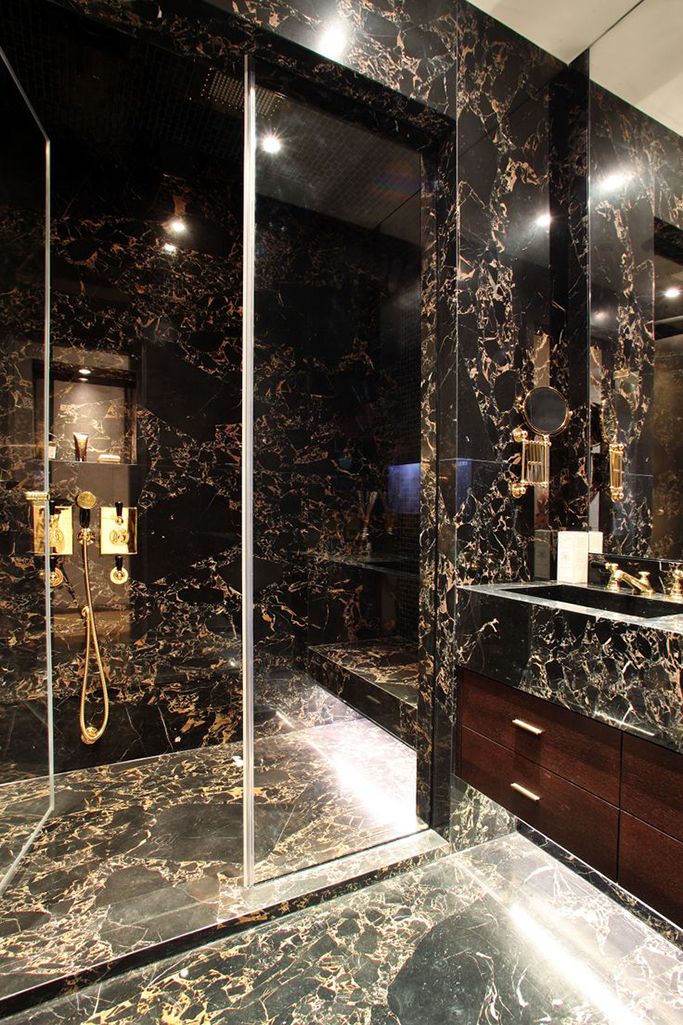 a bathroom with black marble walls and flooring, two sinks and a shower stall