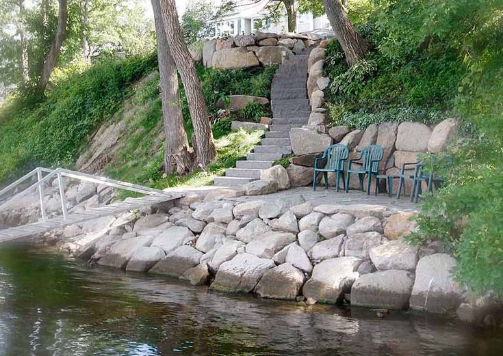 there are two blue chairs sitting on the rocks by the water and stairs leading up to them