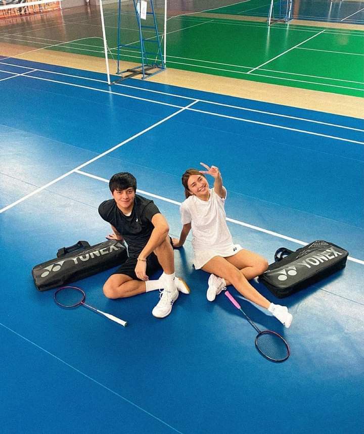 two people sitting on the ground with tennis rackets and bags in front of them