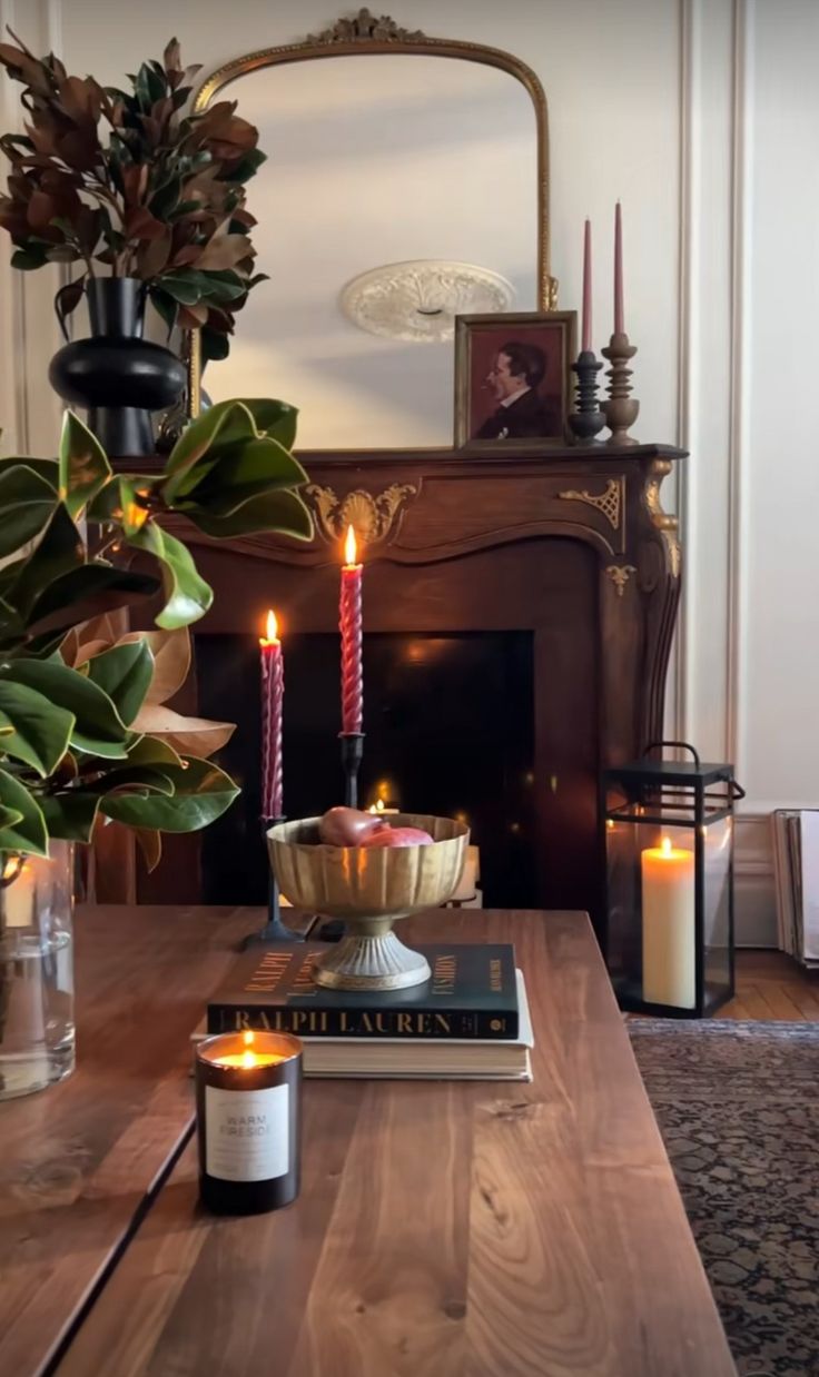 a table with candles and books on it in front of a fire place filled with potted plants