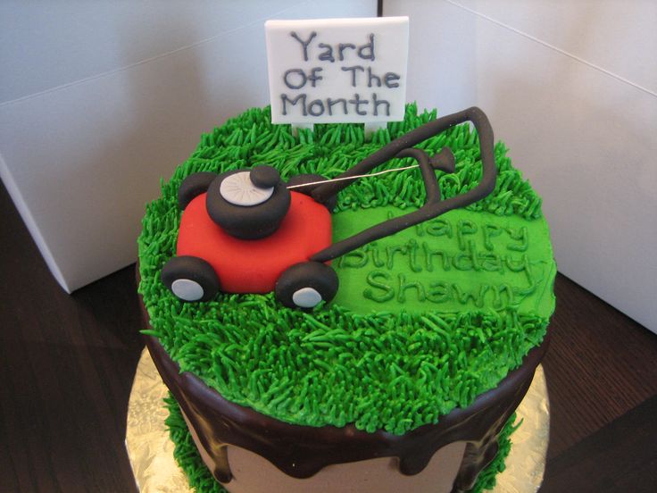 a yard of the month cake with grass and lawn mower on top, sitting in front of a sign that reads yard of the month