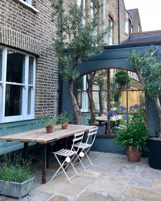 an outdoor dining area with potted plants on the table and chairs in front of it