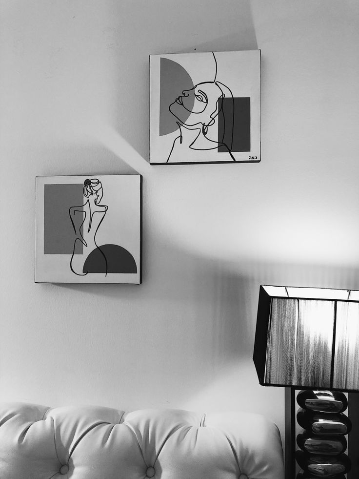 two paintings hang on the wall next to a white couch with a lamp in front of it