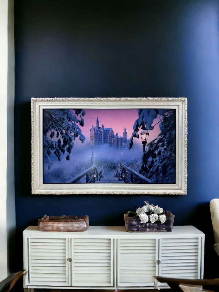 a painting hanging on the wall above a white cabinet in a room with blue walls