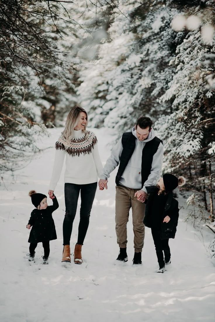 a man and woman holding hands while walking in the snow with two small children on their laps