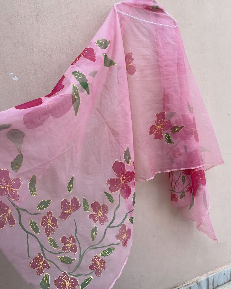 a pink scarf hanging on the side of a white building with flowers painted on it