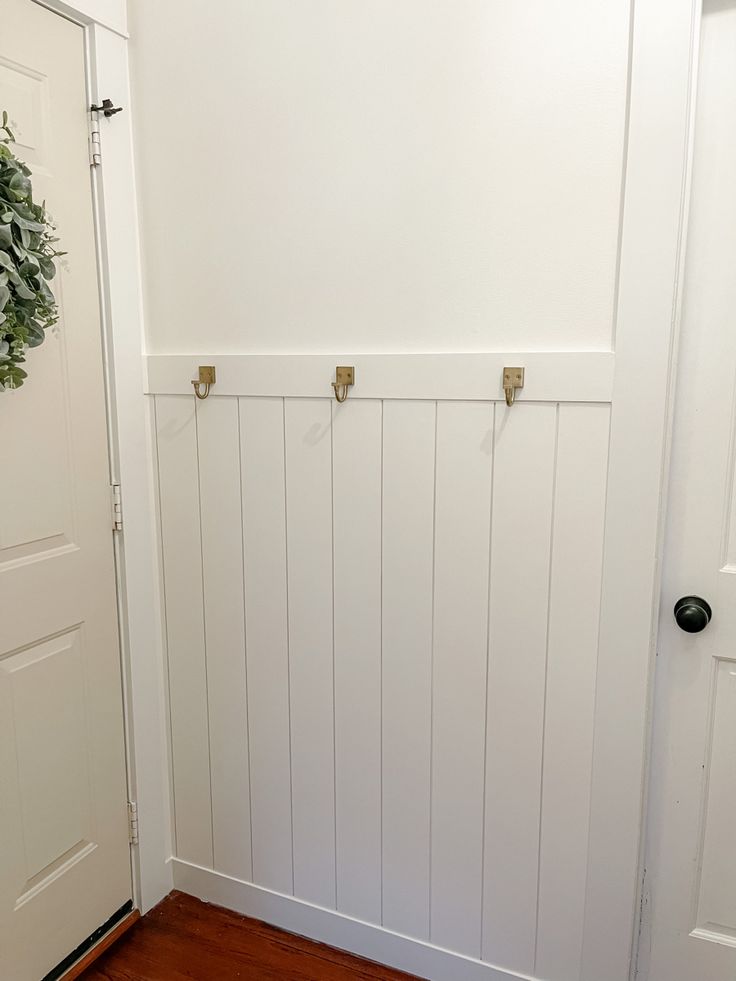 a white door with two hooks and a wreath hanging on the wall next to it