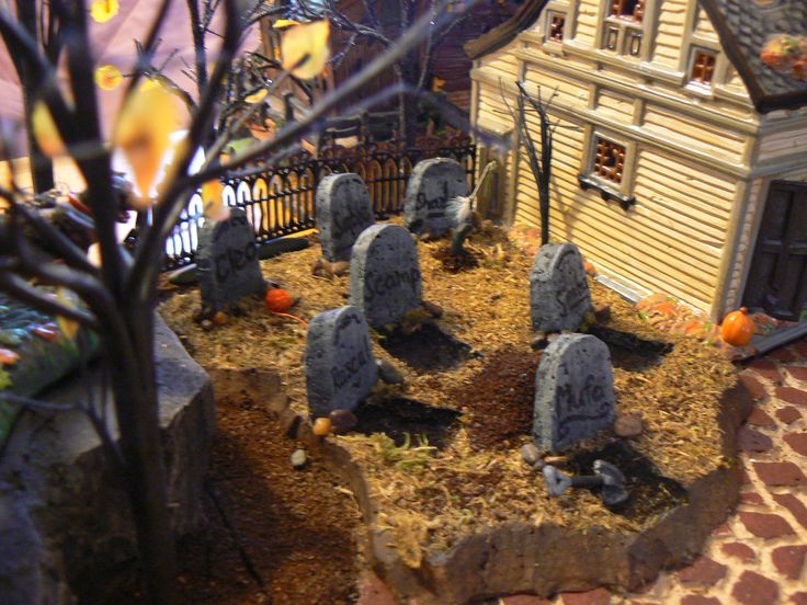 a fake graveyard with tombstones and pumpkins on the ground in front of a house