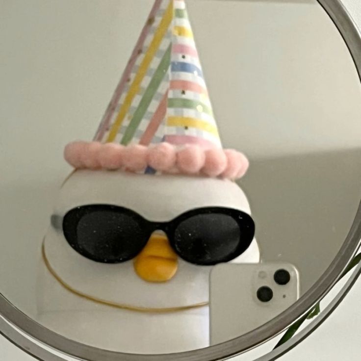 a penguin wearing sunglasses and a party hat is reflected in a mirror on the wall