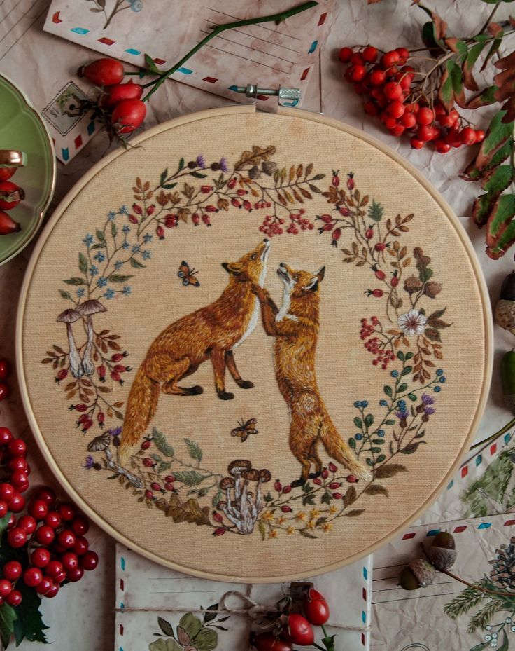 a cross stitch pattern with two foxes in a circle surrounded by berries and holly branches