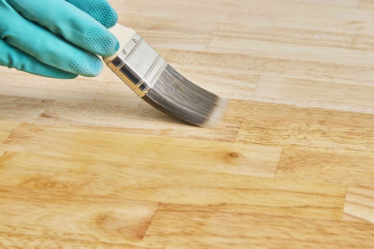 a person in blue gloves is holding a paintbrush on a wooden floor with white and gray stripes