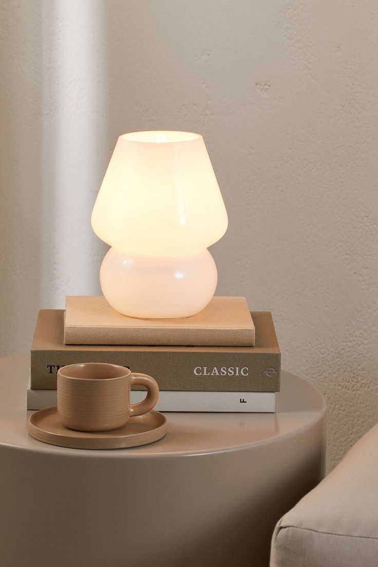 a white lamp sitting on top of a table next to a stack of books and a cup