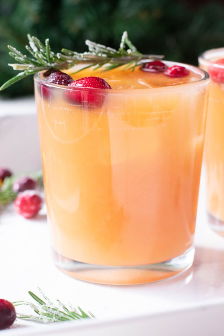 two glasses filled with drinks sitting on top of a white table next to cranberries