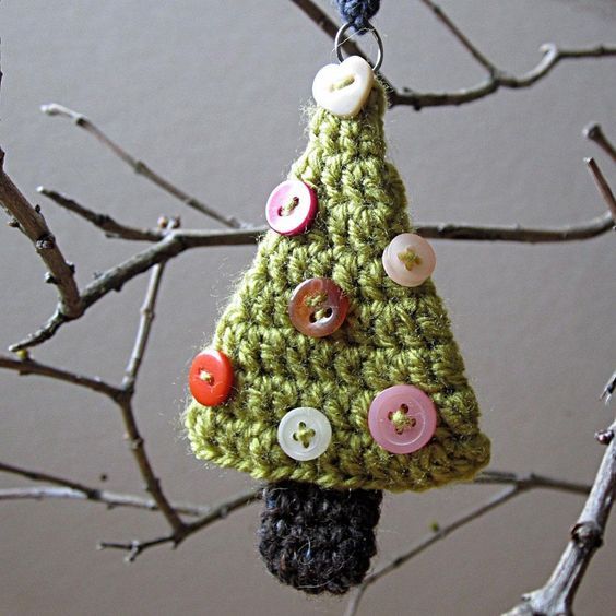 a crocheted christmas tree ornament hanging from a branch with buttons on it