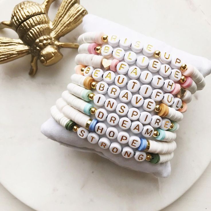 a stack of bracelets sitting on top of a white plate next to a gold brooch