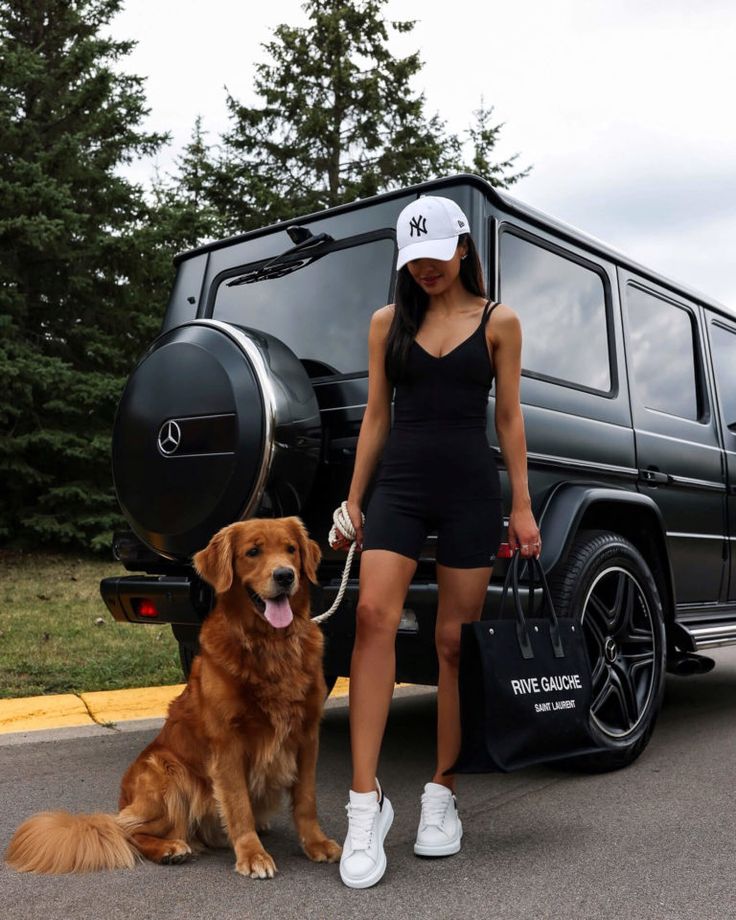 a woman in a black dress and white hat standing next to a brown dog on a leash