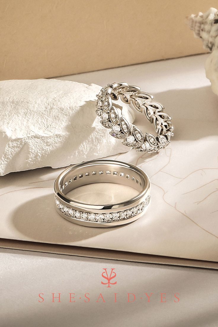 two wedding rings sitting on top of a table next to a napkin and flower vase