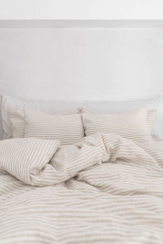 an unmade bed with white linens and striped sheets on it, in a bedroom