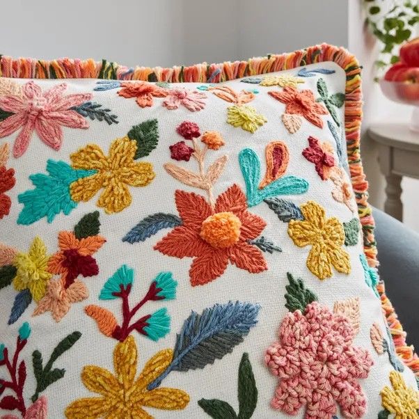 an embroidered pillow with colorful flowers on the front and back, sitting on a chair