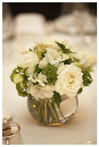 a vase filled with white flowers and greenery on top of a table next to silverware