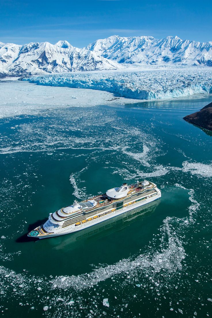 an aerial view of a cruise ship in the water near ice floes and mountains