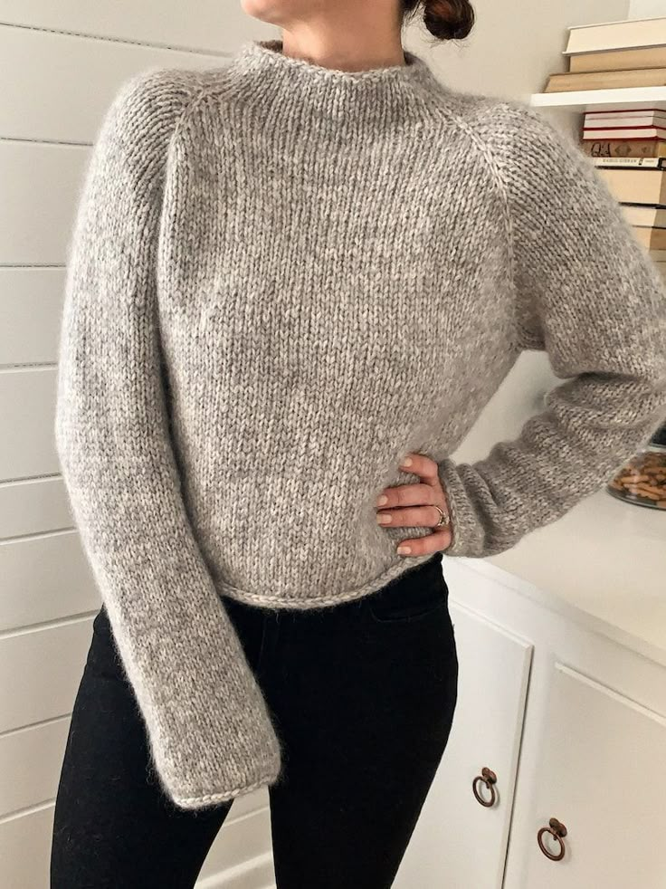 a woman standing in front of a counter wearing a gray sweater and black leggings