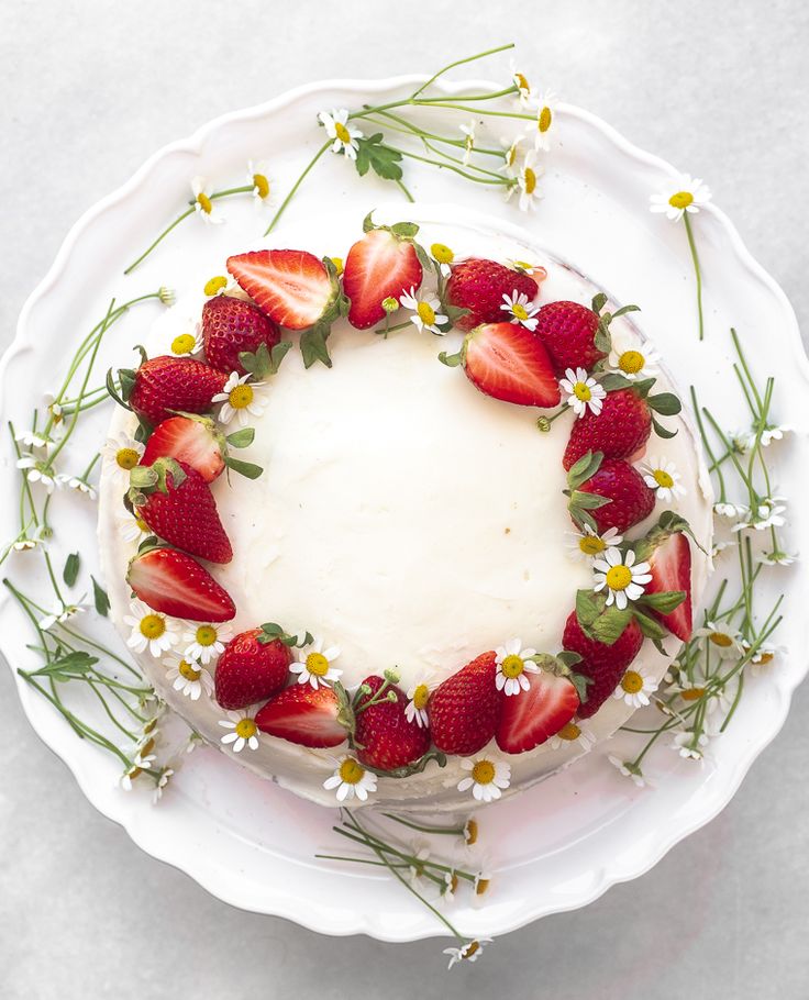 a cake decorated with strawberries and daisies on a white plate in the shape of a wreath