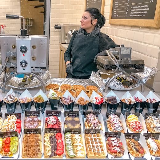 a woman standing in front of a counter filled with lots of different types of food